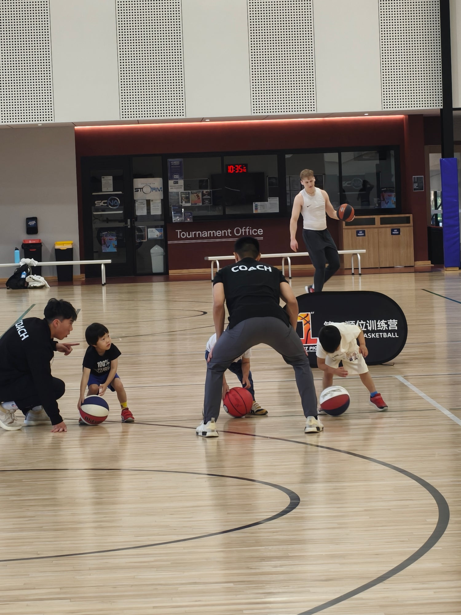Young children in a basketball training session with coaches guiding them on the court