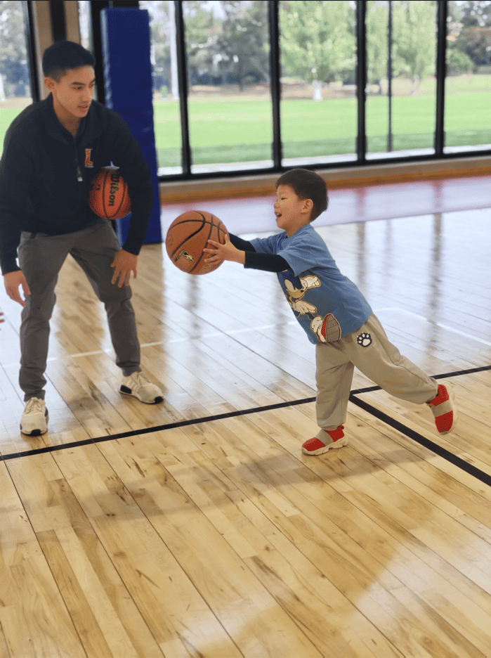 Coach guiding a young child in mini basketball games with positive feedback