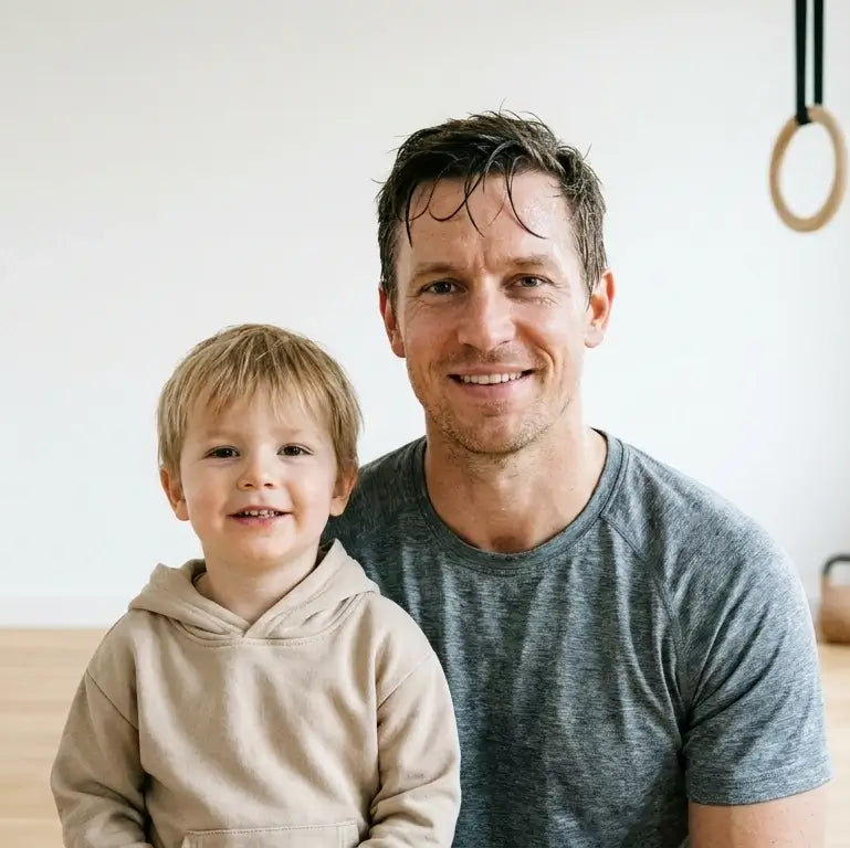 Headshot of fit dad + child in bright minimalist home gym, post-workout relaxed expression, modern neutral activewear, soft studio lighting.