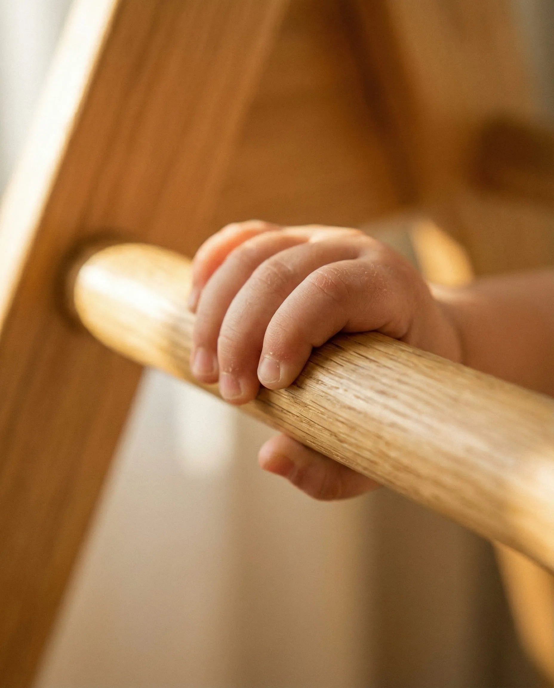 An extreme macro close-up of a young child's hand tightly gripping a smooth, polished wooden rung of a stall bar, demonstrating functional grip strength. Warm golden hour light highlights the natural wood grain, representing the 'Strength' pillar of First Pick's scientific 5+3 development methodology.