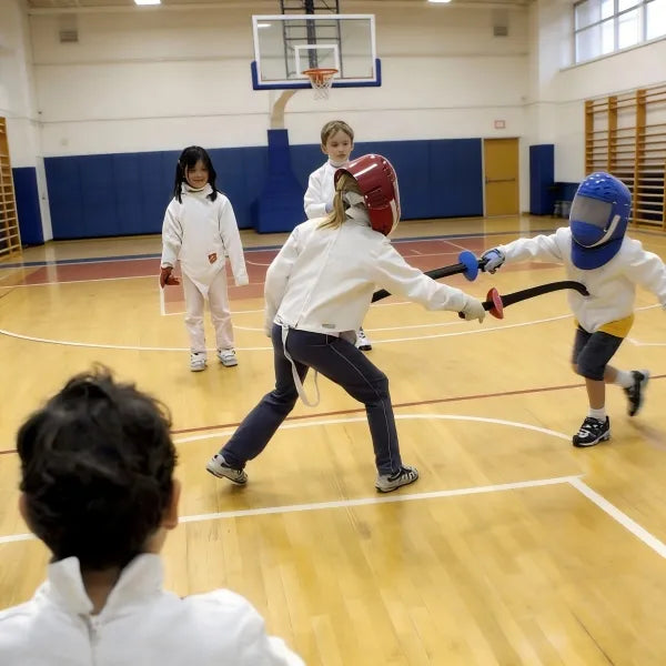 A 4-year-old girl practicing basic fencing moves with a safe foam foil during the Grow & Go multi-sport rotation, focusing on the Reaction and Coordination pillars of the 5+3 system.