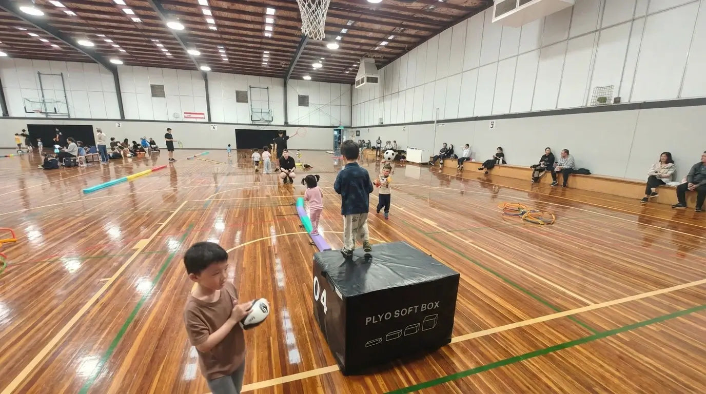 Young children performing neuro-movement drills on a soft plyo box at an indoor sports court, demonstrating the real-world application of the 5+3 Focus System developed by First Pick Academy.