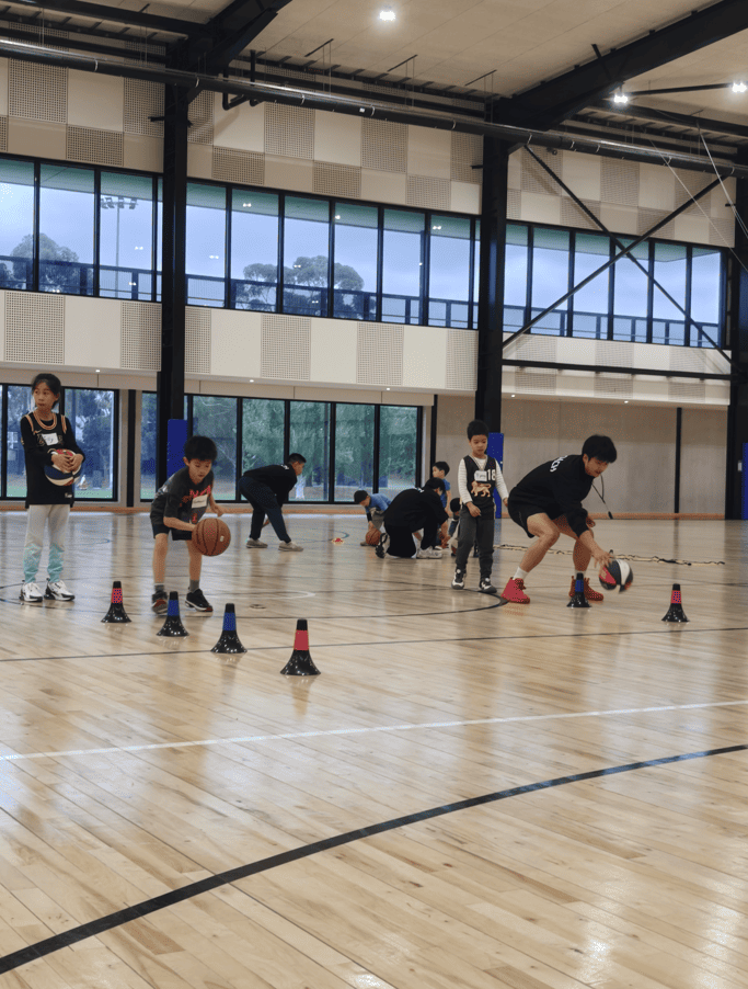 Children practising basketball dribbling drills with cones at First Pick Basketball training in Melbourne indoor court